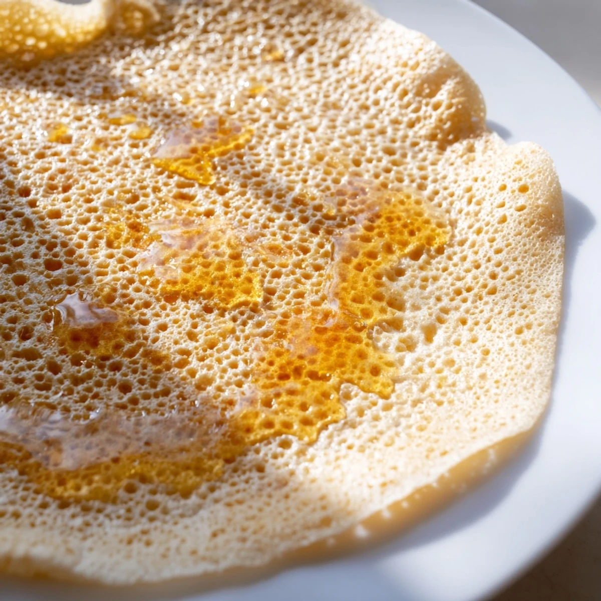 Close-up of a stack of traditional Moroccan Baghrir, showcasing its signature spongy, hole-filled texture.