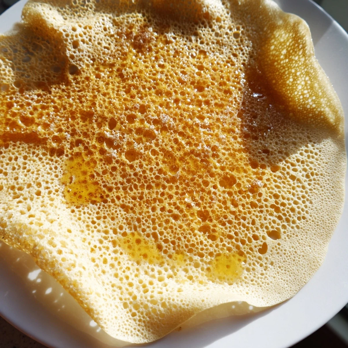 Warm and airy, these homemade Moroccan Baghrir crepes are plated and drizzled with sweet, glossy honey.