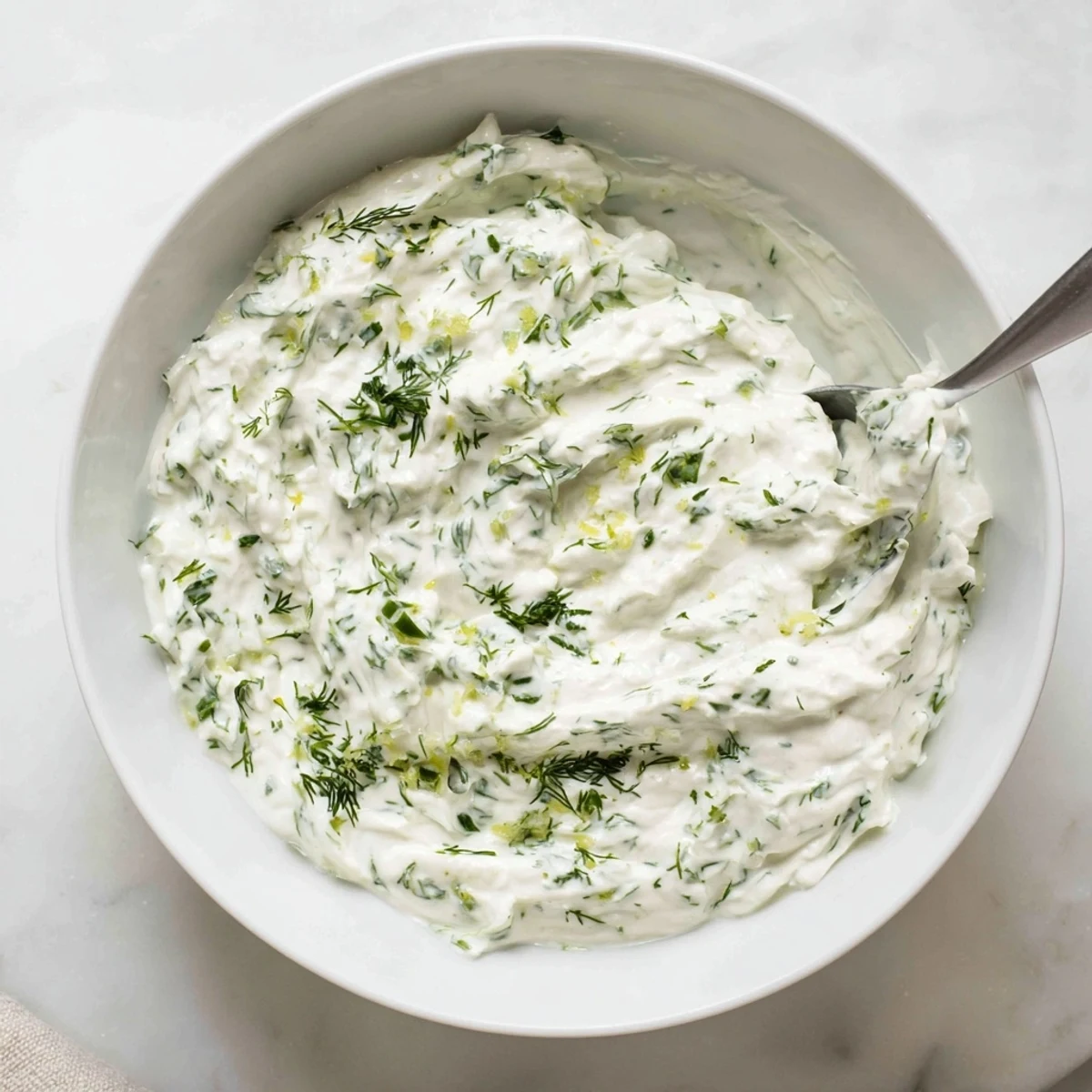 Close-up of a chilled Greek Yogurt Herb Dip next to sliced cucumbers and crunchy carrot sticks, ideal for snacking.