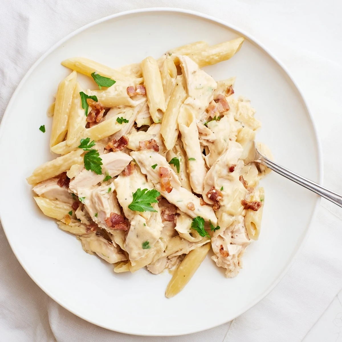 Creamy Chicken Bacon Penne in a skillet, with golden penne tossed in rich Parmesan sauce, topped with crispy bacon and fresh parsley garnish.