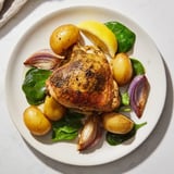 A close-up shot of steaming Pan-Roasted Chicken with Zaatar, alongside roasted potatoes and vibrant greens.