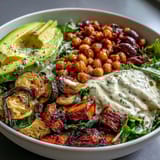 Vibrant Vegan Mediterranean Buddha Bowl with roasted zucchini, creamy avocado, and tangy olives, all drizzled with a zesty tahini dressing.