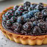 Freshly baked Black Currant Fruit Tart topped with glossy berries and a dusting of powdered sugar.