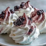 Plated Black Currant Meringues are dusted with deep purple powder, paired with fresh blackberries and a dollop of whipped cream.