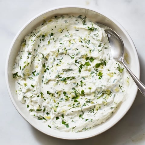 A vibrant bowl of creamy Greek Yogurt Herb Dip garnished with dill, served with fresh vegetable sticks and pita chips for dipping.
