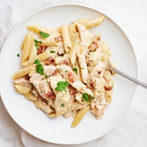 Creamy Chicken Bacon Penne in a skillet, with golden penne tossed in rich Parmesan sauce, topped with crispy bacon and fresh parsley garnish.