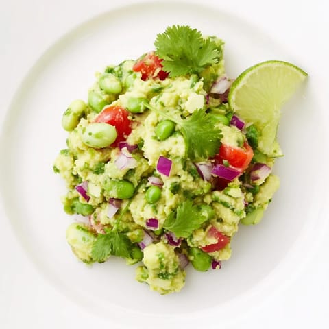 Close-up of fresh Edamame Guacamole garnished with cilantro, ready to be scooped with a chip.