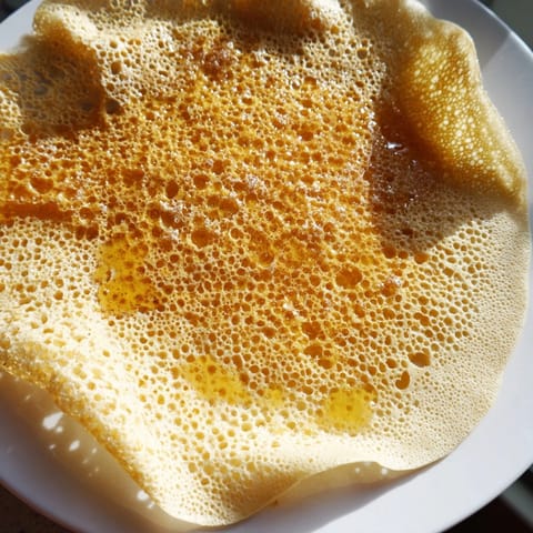 Warm and airy, these homemade Moroccan Baghrir crepes are plated and drizzled with sweet, glossy honey.