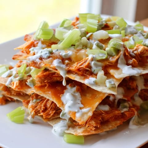 Spicy buffalo chicken nachos with tortilla chips, gooey cheese, and fresh celery garnish, perfect for a game day snack.  
