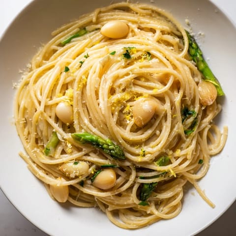 A close-up of Roasted Garlic & Asparagus Pasta, garnished with parsley and lemon zest for brightness.