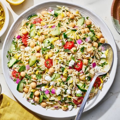 Freshly made Lemony Chickpea Orzo Salad served in a white bowl, showcasing tender orzo, crisp cucumbers, and juicy tomatoes. 