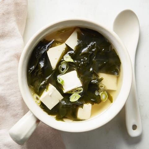 A close-up of vibrant Wakame Soup, featuring soft tofu and green seaweed in a savory Japanese miso broth garnish.