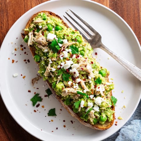 Open-faced Smashed Pea & Chicken Toast topped with crumbled feta and fresh mint, served on a rustic wooden board.