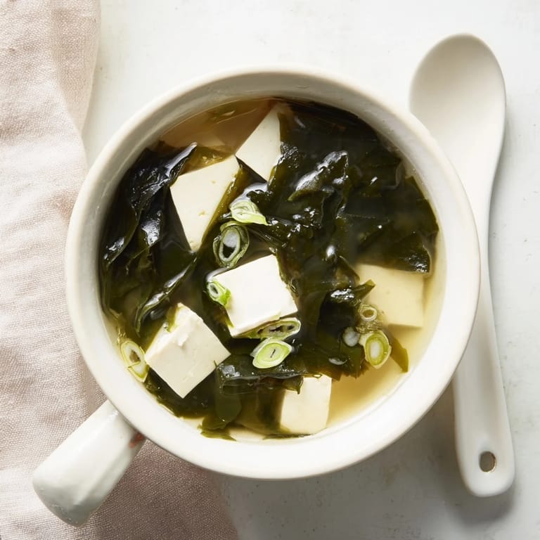 A close-up of vibrant Wakame Soup, featuring soft tofu and green seaweed in a savory Japanese miso broth garnish.