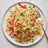 A vibrant bowl of Sauerkraut Slaw with shredded cabbage, grated carrots, and red bell peppers tossed in a light apple cider vinaigrette.