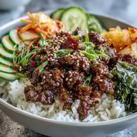 A vibrant Korean Beef Bowl with spicy gochujang ground beef over steamed rice, topped with crisp cucumber and tangy kimchi.  
